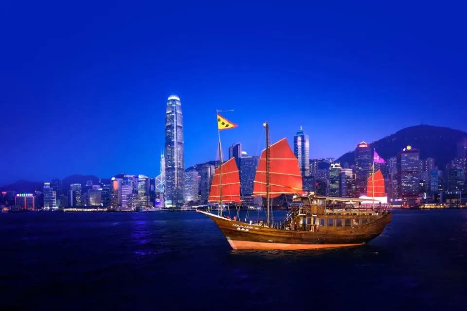 A junk boat in Hong Kong as the city is lit after dark.