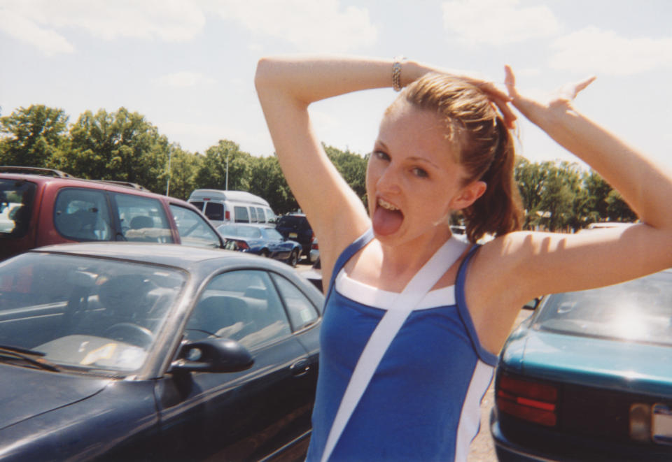 A joyful person poses with hands on their head in a parking lot, expressing a carefree moment