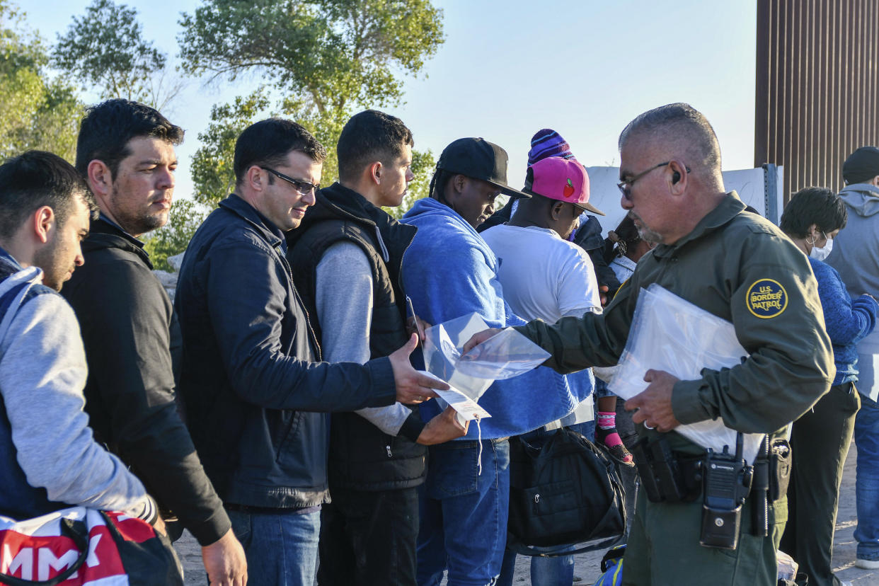 Migrants line up to cross the border, as a U.S. Border Patrol agent hands out forms.