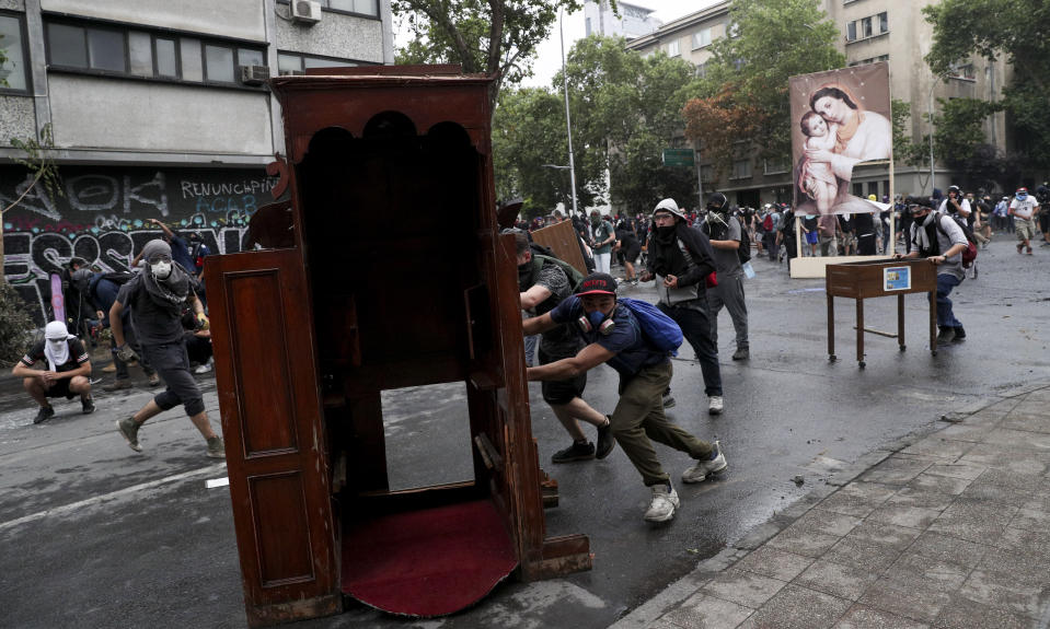 Anti-government protesters drag items from a church to be added to a barricade, in Santiago, Chile, Friday, Nov. 8, 2019. Chile's president on Thursday announced measures to increase security and toughen sanctions for vandalism following three weeks of protests that have left at least 20 dead. (AP Photo/Esteban Felix)