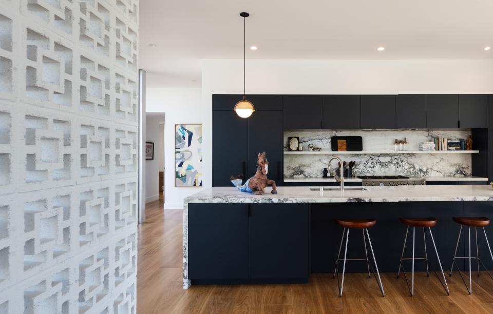 The kitchen is outfitted with Breccia Capraia honed marble tops and cabinets painted in Farrow & Ball’s Railings. Within the backsplash, flush outlets are hand-painted to match the marble. Custom light fixtures by Allied Maker were created specifically for the island.