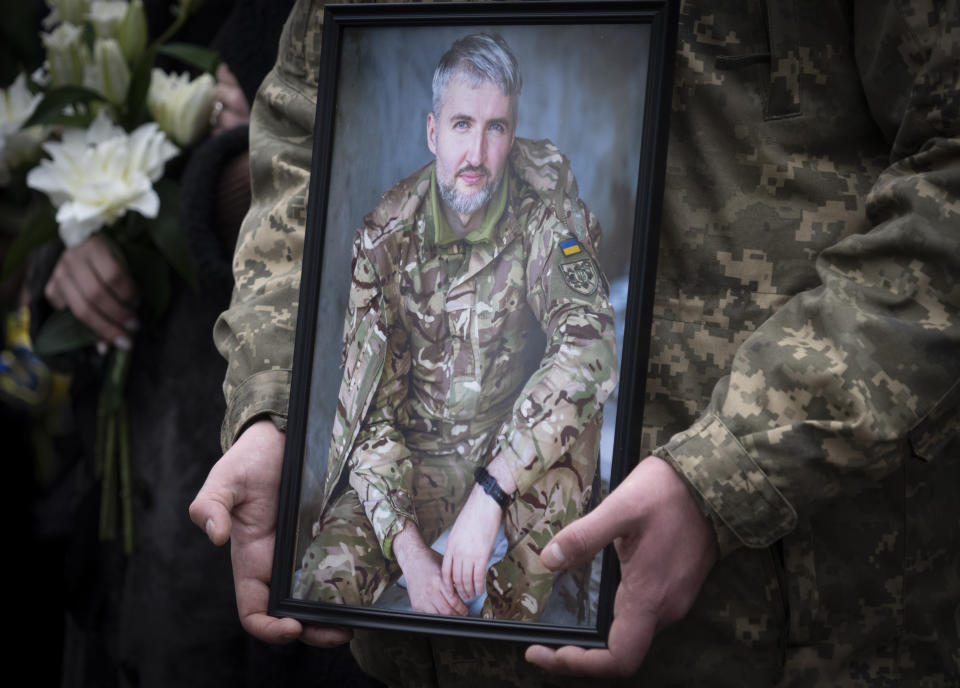 A Ukrainian serviceman holds the photo of his comrade during the funeral ceremony of Volodymyr Yezhov killed in a battlefield with Russian forces at St. Volodymyr Cathedral in Kyiv, Ukraine, Tuesday, Dec. 27, 2022. Yezhov was a game designer in the development of the game Cossacks 2. He was also one of the authors of the game S.T.A.L.K.E.R.: Clear Sky. Yezhov was also one of the most famous Ukrainian e-sportsmen — played StarCraft under the nickname Fresh. Since the Russian invasion, Volodymyr Yezhov went to the frontline and fought as part of the volunteer squadron. (AP Photo/Efrem Lukatsky)