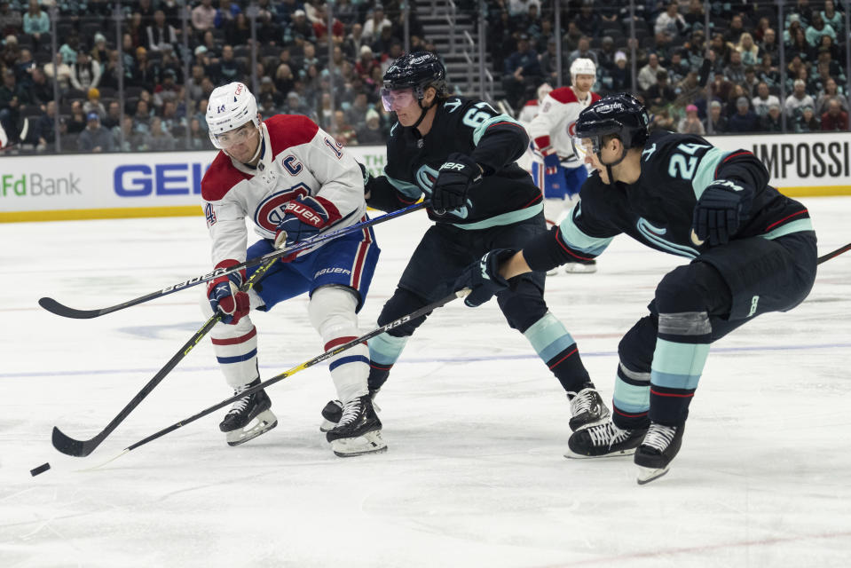 Montreal Canadiens forward Nick Suzuki, left, passes the puck against Seattle Kraken forward Morgan Geekie, center, and defenseman Jamie Oleksiak during the first period of an NHL hockey game, Tuesday, Dec. 6, 2022, in Seattle. (AP Photo/Stephen Brashear)