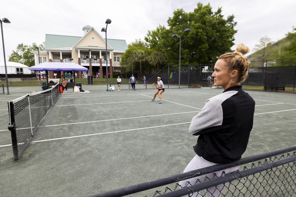 Iris Harris leans on a fence as she watches players on a practice court at the Charleston Open tennis tournament in Charleston, S.C., Monday, April 3, 2023. Harris is a member of the women's professional tennis tour's Coach Inclusion Program to develop female coaches. (AP Photo/Mic Smith)