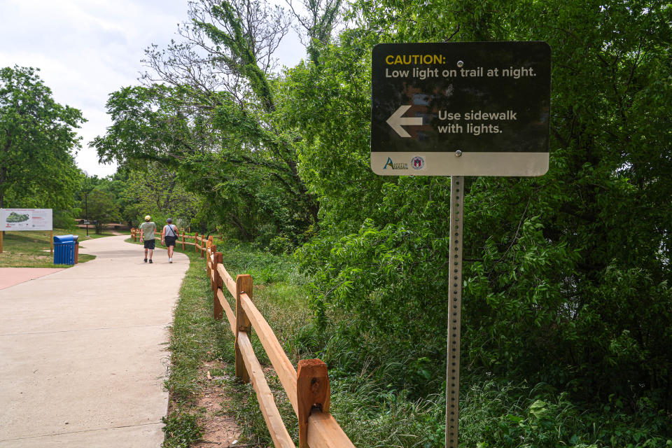 A sign warns of poor lighting conditions at night on a hike-and-bike trail along Lady Bird Lake that passes the end of Rainey Street.