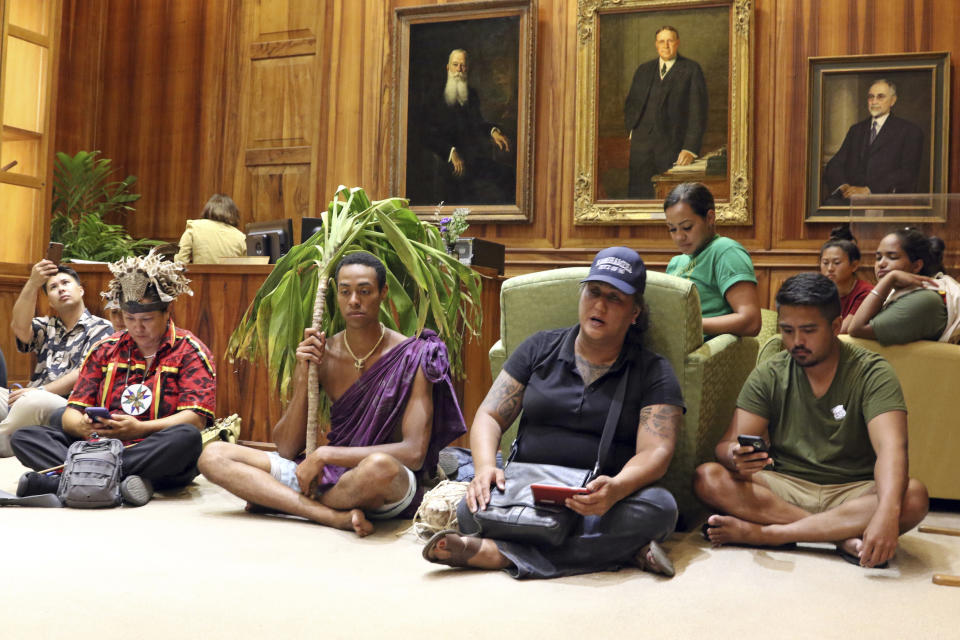 In this Wednesday, July 17, 2019, photo, Hinaleimoana Wong-Kalu, wearing baseball cap, leads protesters in song while sitting on the floor of the reception room at Hawaii Gov. David Ige's office in Honolulu. At left in front row are Kinner Horsen and Kaneali'ikeikioka'aina, while at right in front row is Kainoa McGill. For activists who say they're protecting Mauna Kea, the fight against the proposed Thirty Meter Telescope is a boiling point in Hawaiian history. (AP Photo/Audrey McAvoy)