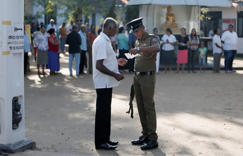 A police officer inspects the polling card of a man before entering into a polling station during the presidential election in Colombo