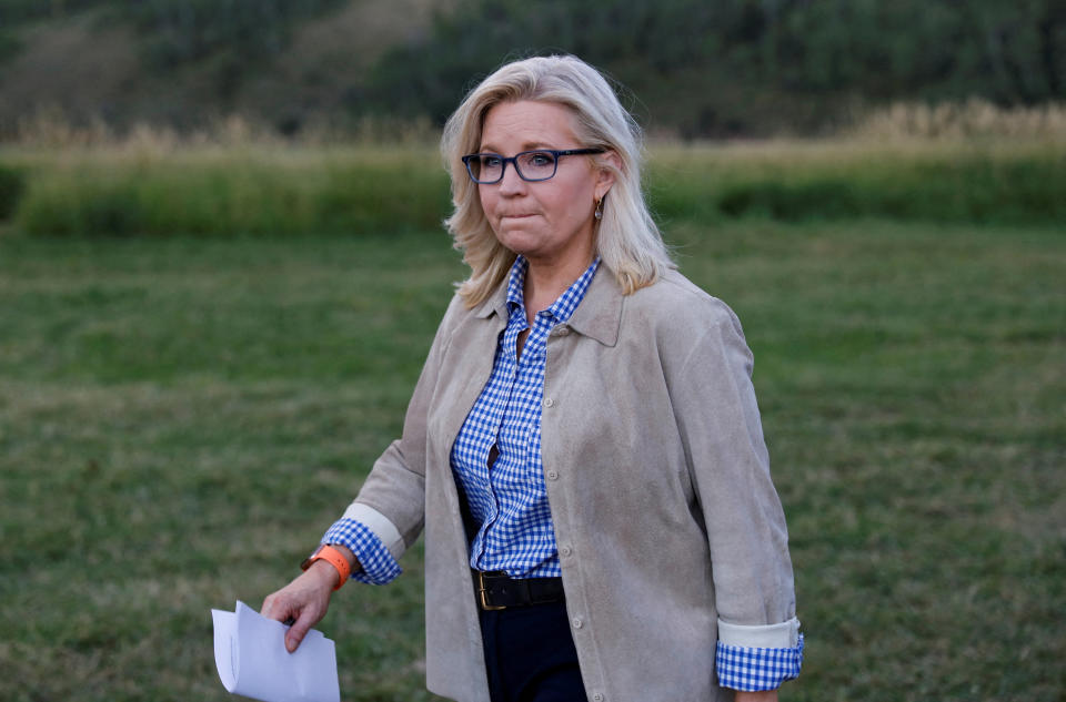 Liz Cheney holds a folded paper and walks across a field.