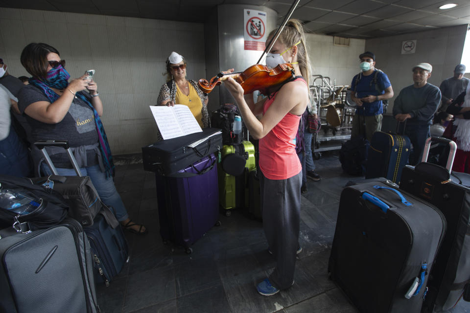 A traveler plays her violin prior to getting on a charter flight coordinated by the U.S. embassy at La Aurora airport in Guatemala City, Monday, March 23, 2020. American citizens stranded abroad because of the coronavirus pandemic are seeking help in returning to the United States. (AP Photo/Moises Castillo)