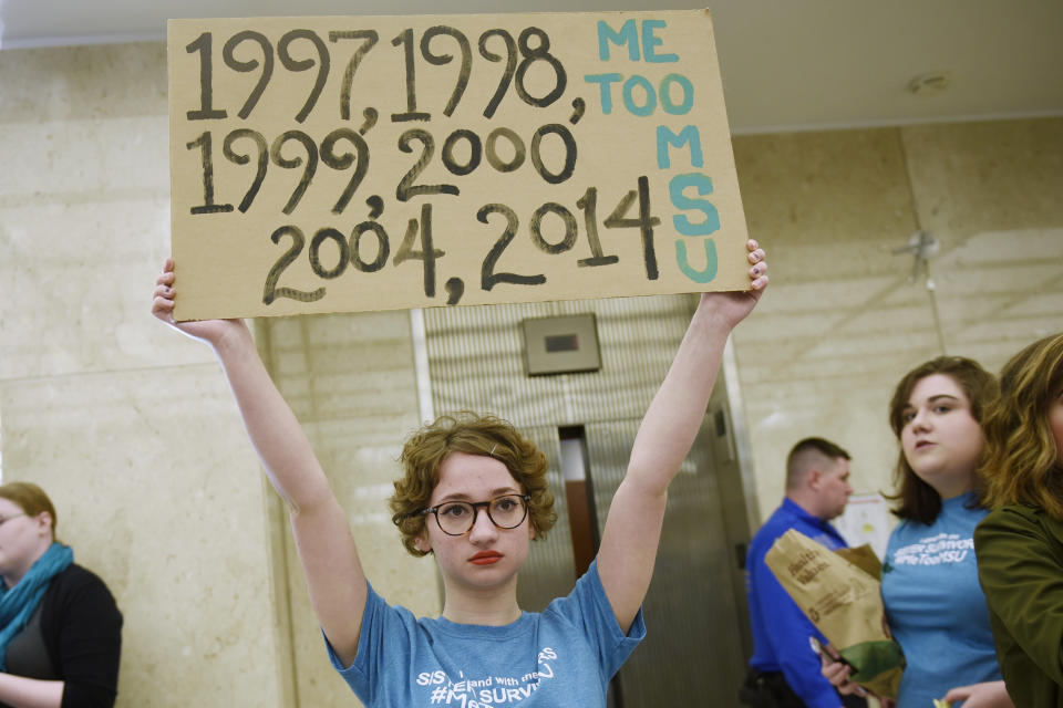 FILE - In this April 13, 2018 file photo, Morgan McCaul, 18, a survivor of Larry Nassar abuse, holds a sign showing the years that Larry Nassar was reported to Michigan State University as trustees arrive for a university board meeting. The government's $4.5 million fine against Michigan State University in the Nassar sexual assault scandal is unprecedented. The U.S. Education Department has extraordinary leverage over schools that participate in federal student aid programs. (Clarence Tabb Jr./Detroit News via AP, File)