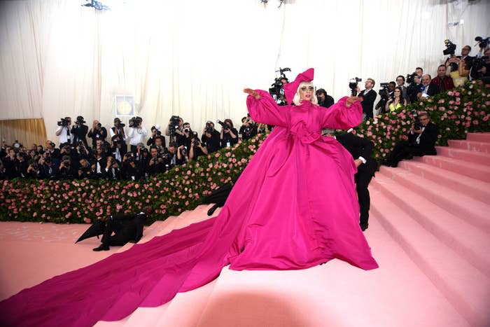 Lady Gaga in a voluminous pink gown with a long train, posing on stairs at an event