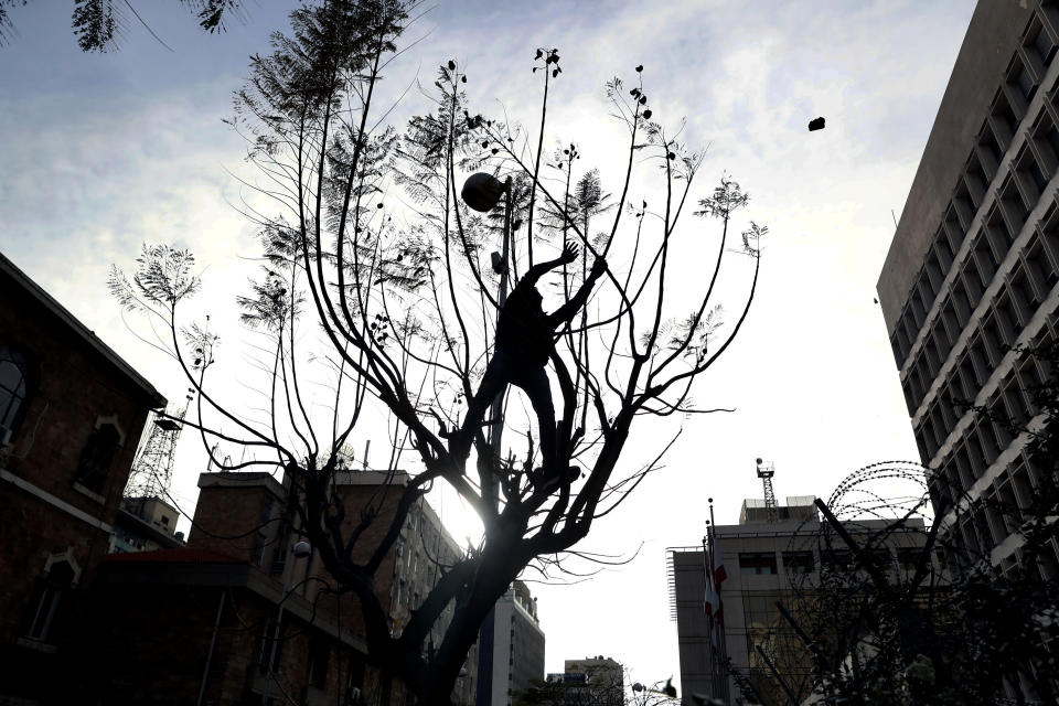 A protester on a tree throws stones towards the central bank building, during a protest in Beirut, Lebanon, Saturday, March. 13, 2021. Riot police fired tear gas to disperse scores of people who protested near parliament building in central Beirut Saturday amid deteriorating economic and financial conditions and as the local currency hit new low levels (AP Photo/Bilal Hussein)