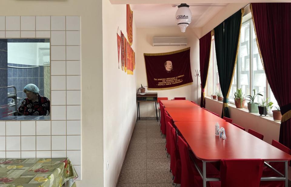 A long red table surrounded with red chairs sits in a cafe with mostly red wall hangings against white walls