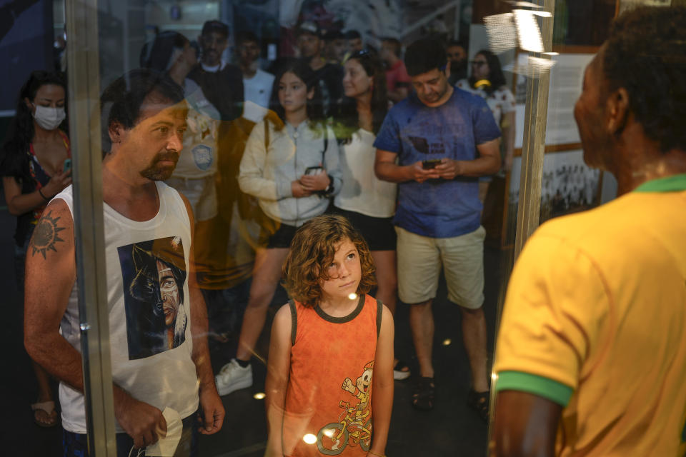 Los visitantes al Museo Pele en Santos, Brasil, observan una estatua de tamaño natural de Pelé, con una camiseta amarilla brillante de la selección de Brasil, exhibida en una vitrina el viernes 30 de diciembre de 2022. Pelé, quien jugó la mayor parte de su carrera con Santos FC, falleció en un hospital de Sao Paulo el jueves a la edad de 82 años. (AP Foto/Matias Delacroix)