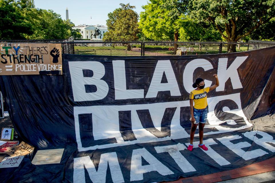 A young woman holds her fist up in front of a large banner hanging on a security fence at 16th and H Street in Washington on June 8, 2020, after days of protests over the death of George Floyd, a black man killed by police in Minneapolis. The barrier came to be known as the Black Lives Matter Memorial Fence.