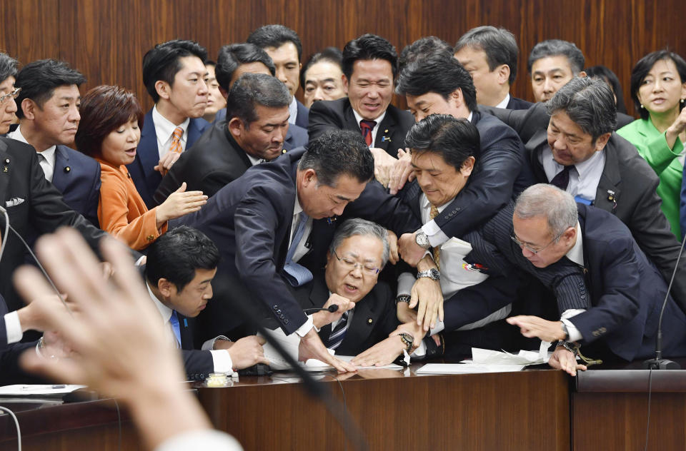Japan's opposition parties' members try to stop Judicial Affairs Committee Chairman Shinichi Yokoyama, bottom center, from moving to hold a vote for a bill to revise an immigration control law, at upper house committee in Tokyo early Saturday, Dec. 8, 2018. Japan is preparing to officially open the door to foreign workers to do unskilled jobs and possibly eventually become citizens. (Yoshitaka Sugawara/Kyodo News via AP)