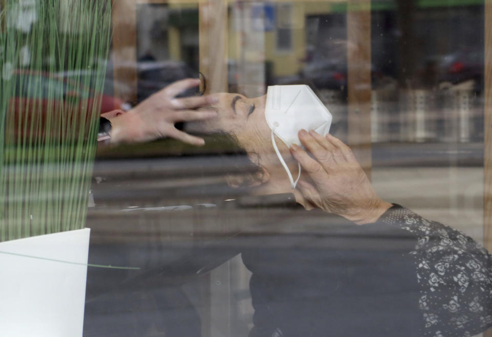 A woman with a mask is at a hairdresser after lock down in Vienna, Austria, Monday, Feb. 8, 2021. Photographed through a pane of glass. The Austrian government has moved to restrict freedom of movement for people, in an effort to slow the onset of the COVID-19 coronavirus. (AP Photo/Ronald Zak)