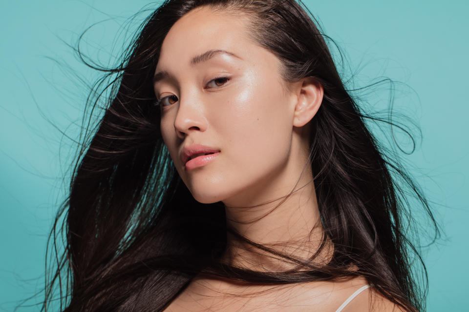 Close up portrait of beautiful young woman with perfect and clean skin. Model with hair flying looking at camera against blue background.