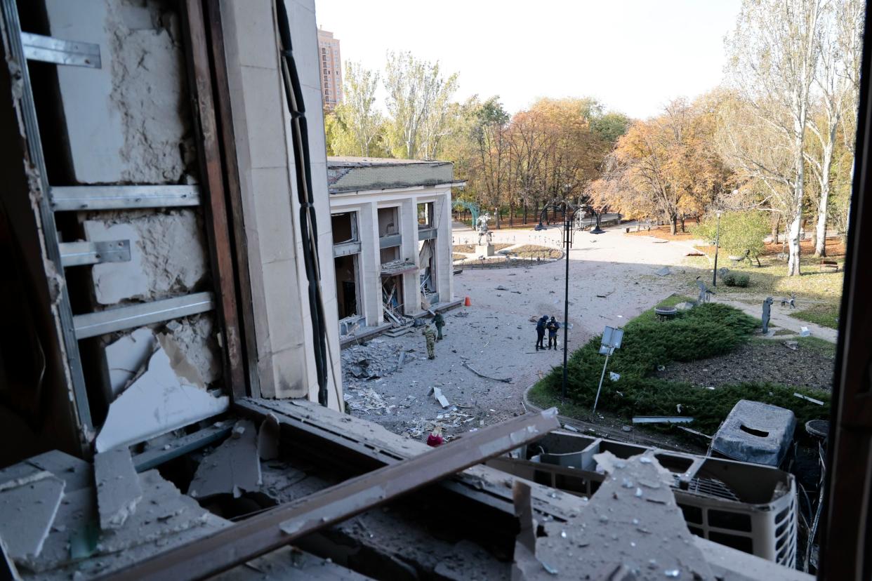 Investigators are seen through a broken window as they work at the site of the damaged administrative building after shelling in Donetsk, the capital of Donetsk People's Republic, eastern Ukraine, Sunday, Oct. 16, 2022. 