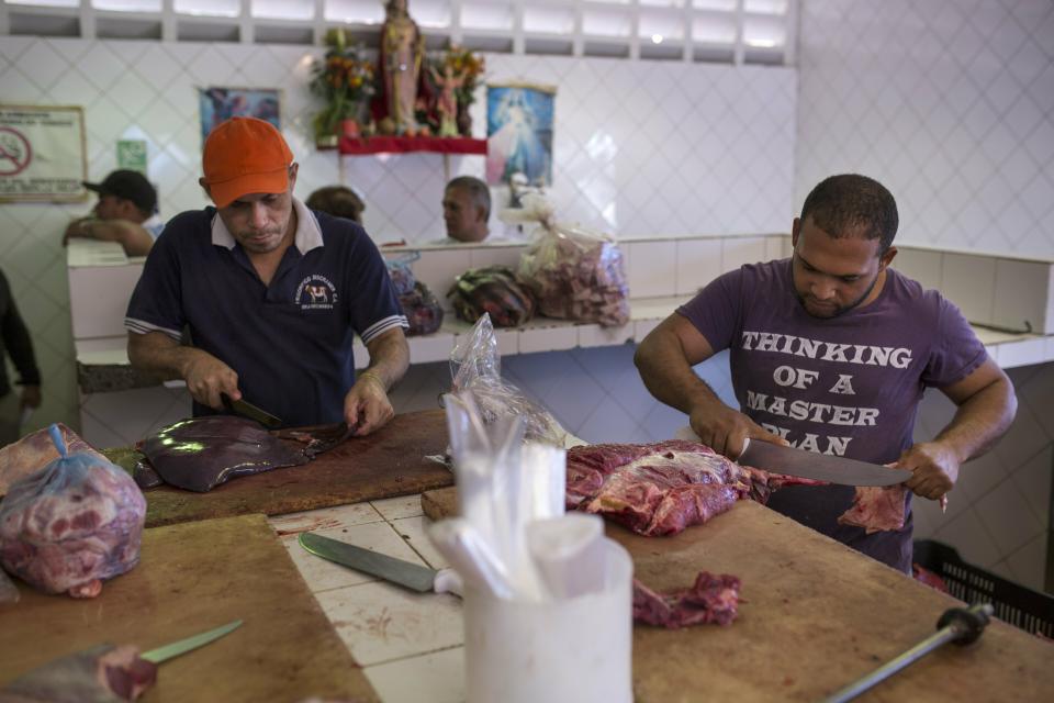 Butchers cut meat at a wholesale food market in Caracas, Venezuela, Monday, Jan. 28, 2019. Economists agree that the longer the standoff between the U.S.-backed opposition leader Juan Guaido and President Nicolas Maduro drags on, the more regular Venezuelans are likely to suffer. (AP Photo/Rodrigo Abd)