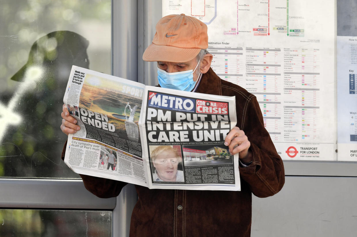 A man wearing a facemask at a bus stop reading a newspaper outside St Thomas' Hospital in Central London where Prime Minister Boris Johnson is in intensive care as his coronavirus symptoms persist.