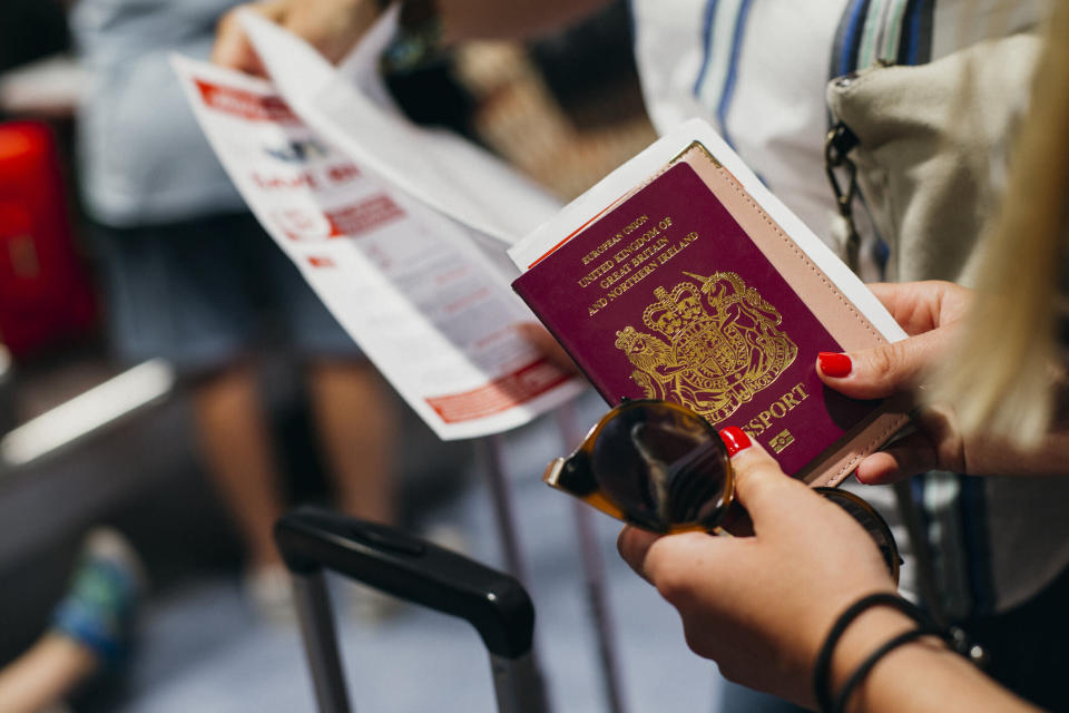 Close-up shot of a mid-adult woman holding a UK passport in her hand while waiting in the airport terminal.