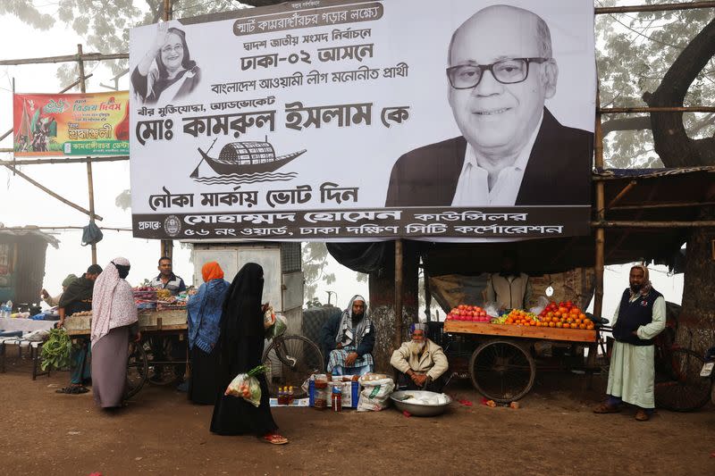 Vendors sell fruits and vegetables under an election campaign banner ahead of the general election in Dhaka