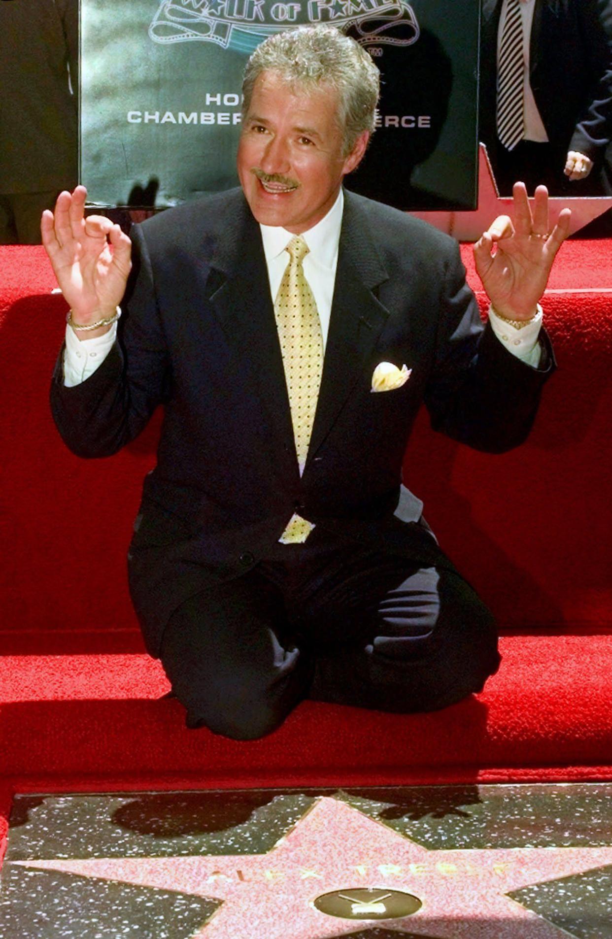 Emmy award-winning game show host Alex Trebek gestures to the 400 fans on hand to watch him receive his newly-dedicated star on the Hollywood Walk of Fame in Los Angeles on May 17, 1999.