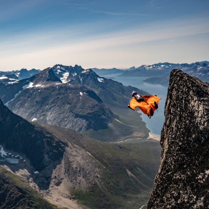 The jumper right after setting off from a grassy cliff top, fiords in background. 