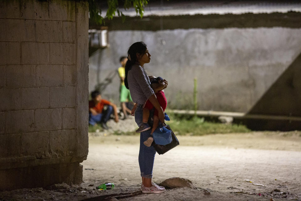 A woman holds a child near a crime scene as forensic workers inspect a body on the street in the Rivera Hernandez neighborhood of San Pedro Sula, Honduras, on Nov. 30, 2019. (AP Photo/Moises Castillo)