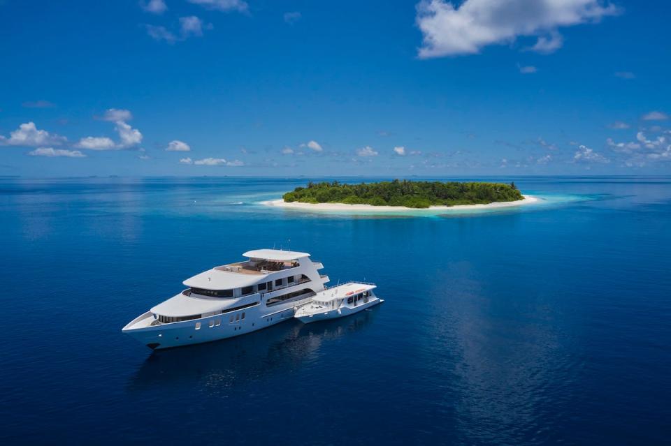 A yacht and smaller boat in the ocean with an island in the distance.