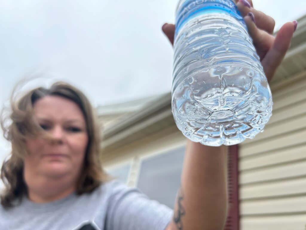Misty Livingston-Holmes holds up a bottle of water filled from the spout outside her home. Black flecks she says are manganese float at the bottom. Livingston-Holmes and neighbors have been struggling with poor water quality and inconsistent bills.