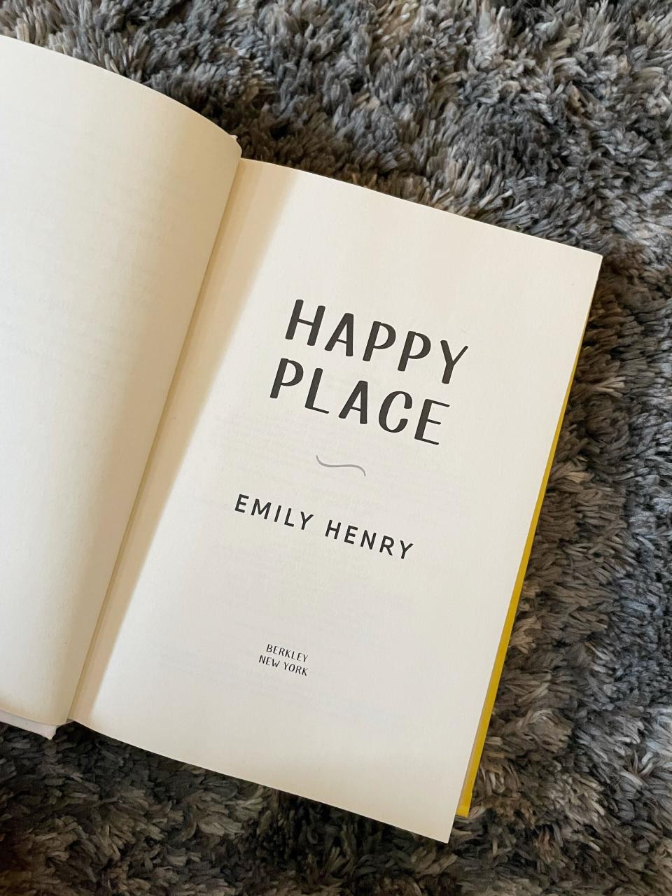 The author is showing off a copy of Emily Henry's "Happy Place"