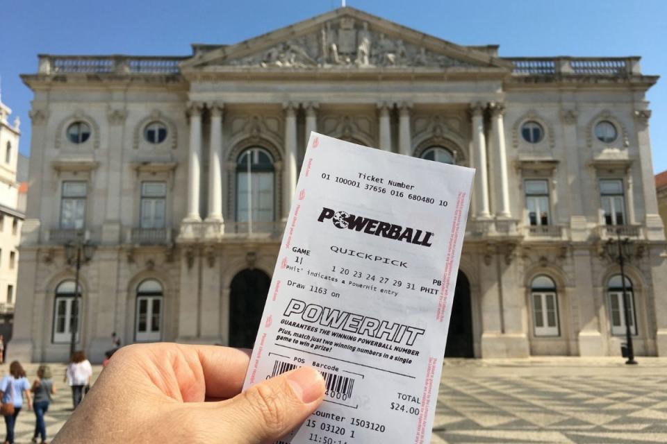 Powerball division one winner holds winning PowerHit ticket up while travelling