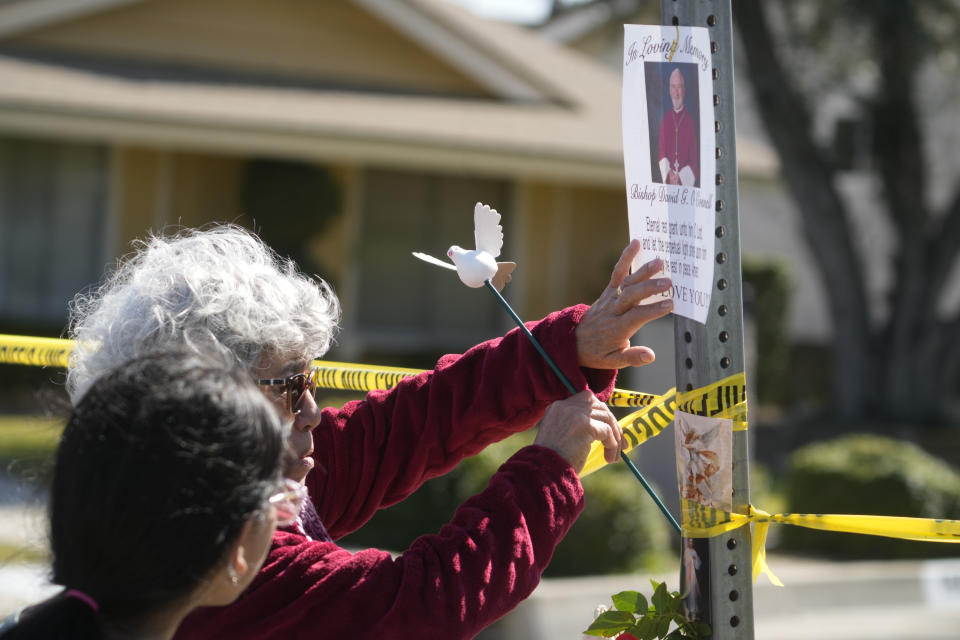 Rosa Maria Perez, with her granddaughter Abigail Gil, pay their respects to Bishop David O'Connell at the corner of his home in Hacienda Heights, Calif., Sunday, Feb. 19, 2023. According to the Los Angeles County Sheriff's Department, detectives are investigating the death of O’Connell, who was shot and killed Saturday just blocks from a church, as a homicide. (AP Photo/Damian Dovarganes)