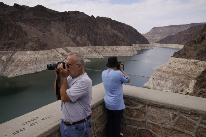 People take pictures of Lake Mead near Hoover Dam at the Lake Mead National Recreation Area, Friday, Aug. 13, 2021, in Arizona. The bathtub ring of light minerals shows the high water mark of the reservoir which has fallen to record lows. (AP Photo/John Locher)