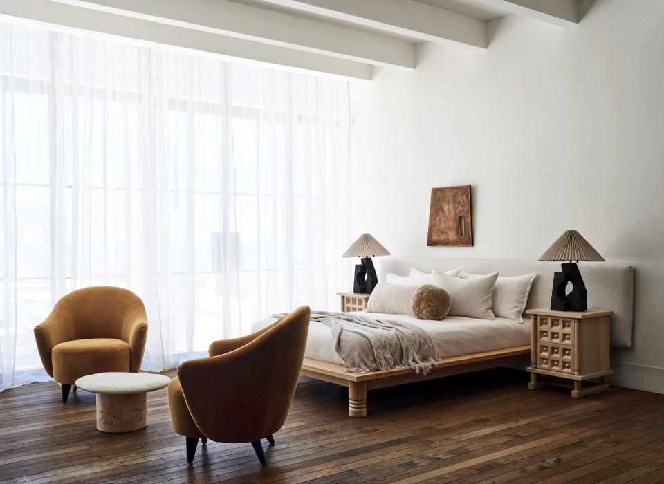 A neutral bedroom with wooden floors, orange velvet chairs, bed and wooden carved bedside table