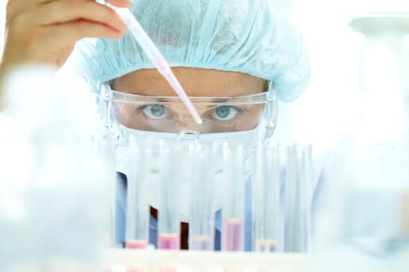 A pharmaceutical lab technician using a pipette to put liquid into test tubes.