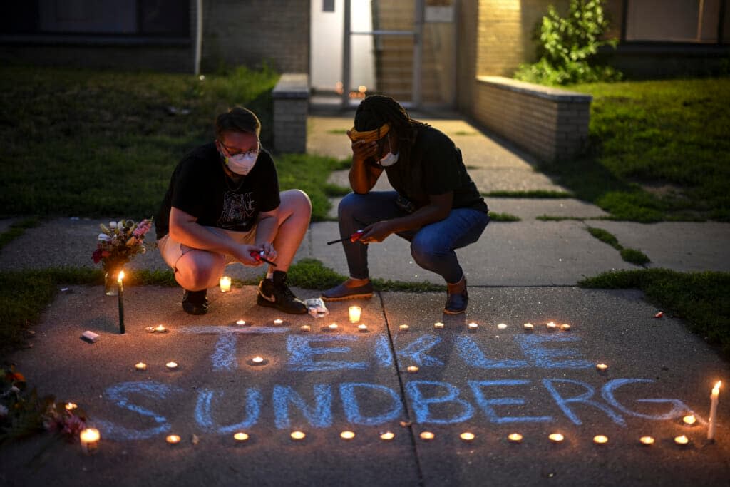 Marcia Howard, activist and George Floyd Square caretaker, right, takes a moment as she lights candles during a vigil for 20-year old Andrew Tekle Sundberg Thursday, July 14, 2022 outside the apartment building where he was killed by Minneapolis Police in Minneapolis. (Aaron Lavinsky/Star Tribune via AP)