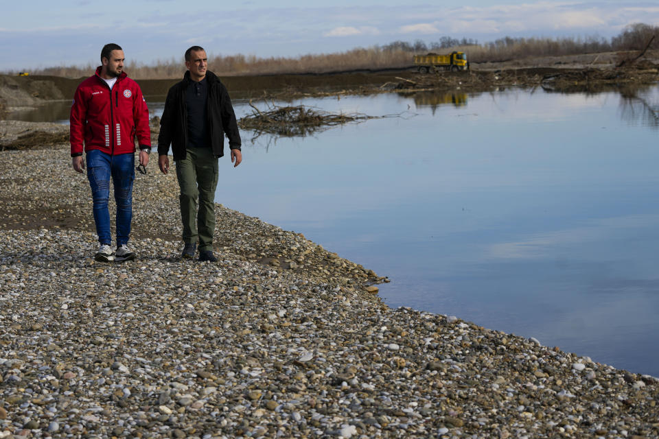 Mountain Rescue Service members Mladen Rosic, left, and Nenad Jovanovic walk along a bank of the Drina River near the village of Amajlije, eastern Bosnia, Sunday, Feb. 4, 2024. In several cities along this river between Bosnia and Serbia, simple, durable gravestones now mark the final resting places of dozens of refugees and migrants who drowned in the area while trying to reach Western Europe.(AP Photo/Darko Vojinovic)