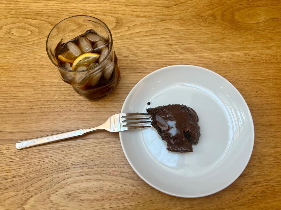 A plate with a piece of chocolate cake and a fork next to a glass of soda with ice and lemon.