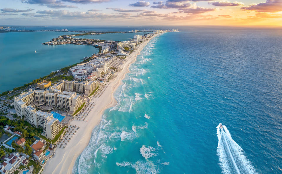 Aerial view of a luxury beachfront resort area in Cancun, Mexico with white sand beaches, turquoise water, high-rise hotels, and a speedboat on the ocean