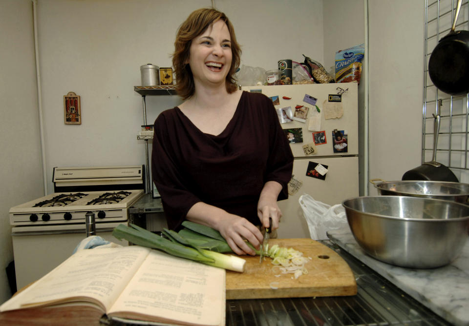 FILE - Food writer Julie Powell chops leeks to make potato leek soup, one of the first recipes in Julia Child's "Mastering the Art of French Cooking," shown at left, in her apartment in New York on Sept. 30, 2005. Powell, who became an internet darling after blogging for a year about making every recipe in Child’s book, leading to a book deal and a film adaptation, died of cardiac arrest on Oct. 26, 2022, at her home in upstate New York. She was 49. (AP Photo/Henny Ray Abrams, File)