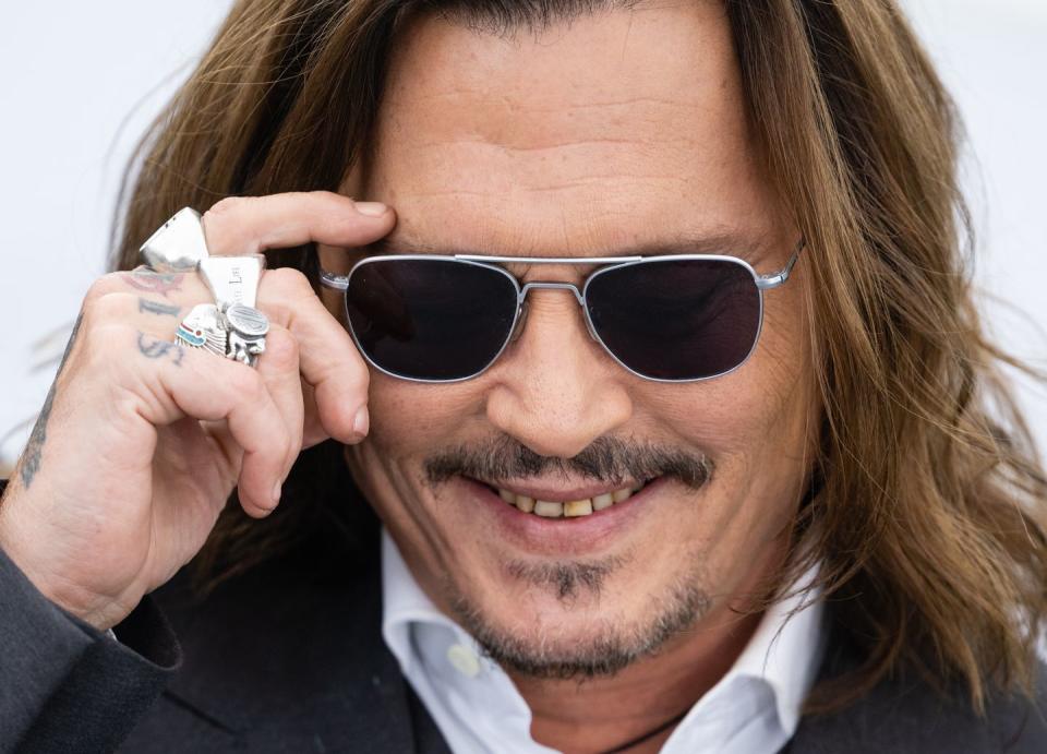 johnny depp smiling as he moves his hand to adjust his sunglasses at an event