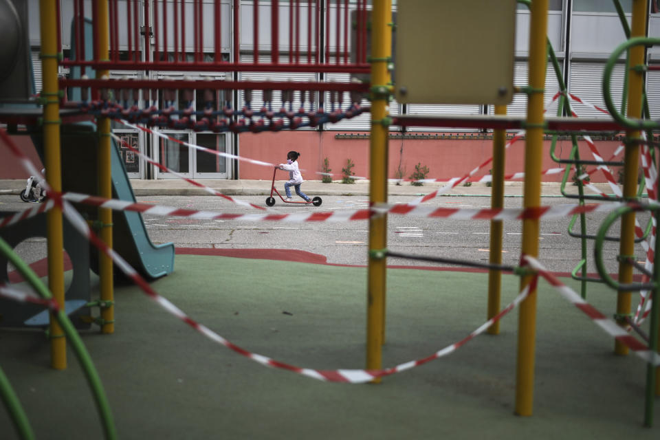 A girl rides a scooter by a prohibited playground in the schoolyard of the Saint-Tronc Castelroc primary school in Marseille, southern France, Thursday, May 14, 2020. The school can only operate three classroom since the others could not be disinfected. The government has allowed parents to keep children at home amid fears prompted by the COVID-19. (AP Photo/Daniel Cole)