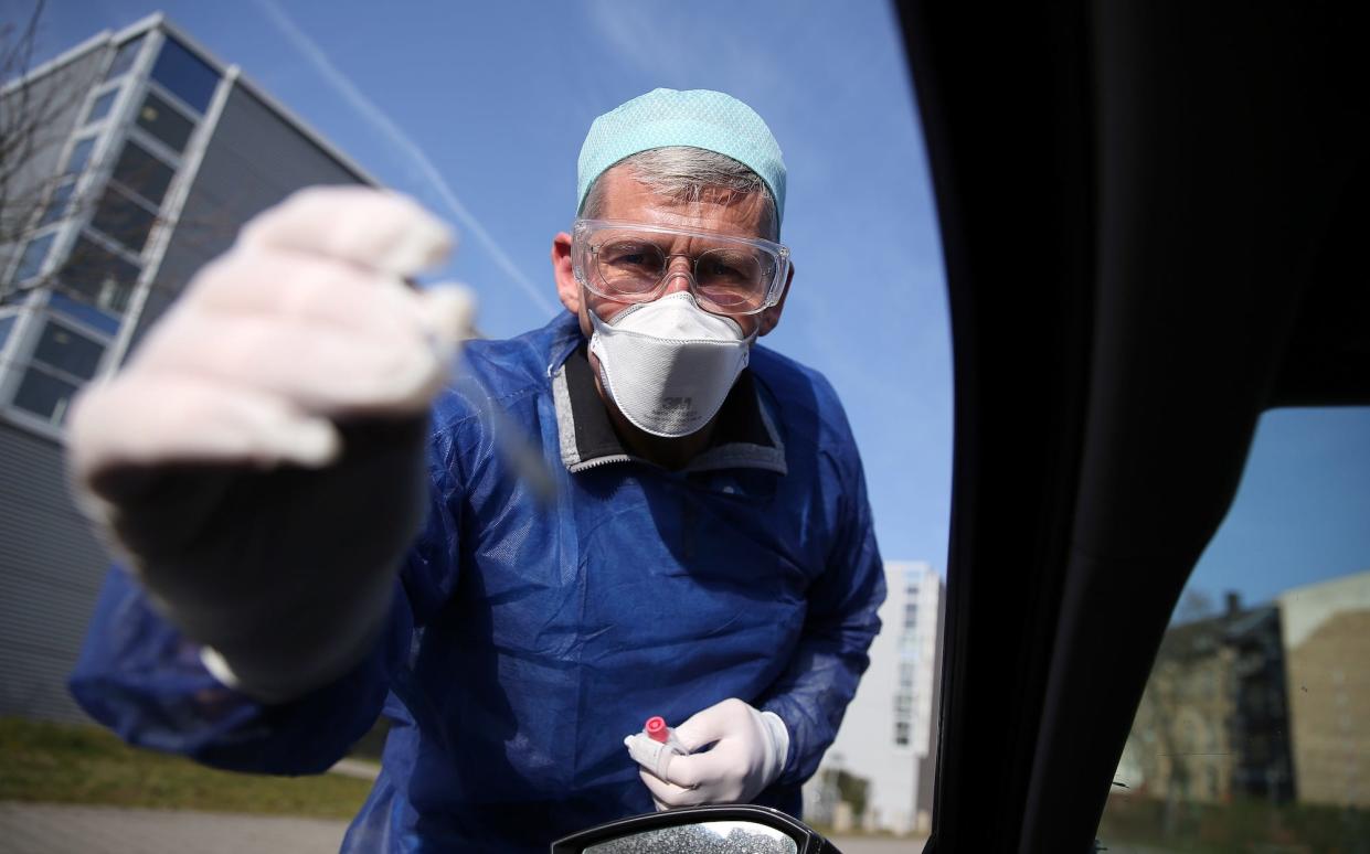 German doctor Michael Grosse takes a sample from a car driver through the window on March 27, 2020 at a drive through testing point for the novel coronavirus on a parking in Halle, eastern Germany. - German researchers plan to regularly test over 100,000 people to see if they have overcome infection with COVID-19 to track its spread, an institute behind the plan confirmed on March 27, 2020. (Photo by Ronny Hartmann / AFP) (Photo by RONNY HARTMANN/AFP via Getty Images)