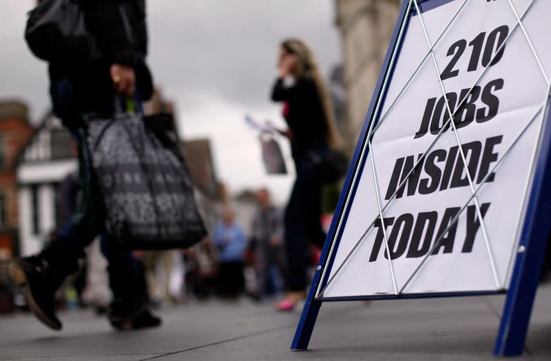 Shoppers walk past a newspaper advertising board promoting its job supplement in Leicester, central England