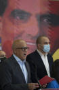 Venezuelan President of the National Assembly Jorge Rodriguez, left, speaks to the press as an image of Colombian businessman and Venezuelan special envoy Alex Saab is in the back in Caracas, Venezuela, Saturday, Oct. 16, 2021. Venezuela’s government said Saturday it would halt negotiations with the country's opposition in retaliation for the extradition to the U.S. of a close ally of President Nicolás Maduro wanted on money laundering charges. (AP Photo/Ariana Cubillos)