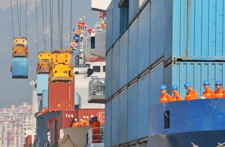 Workers look at cranes lifting containers onto cargo vessels at a port in Yantai, Shandong