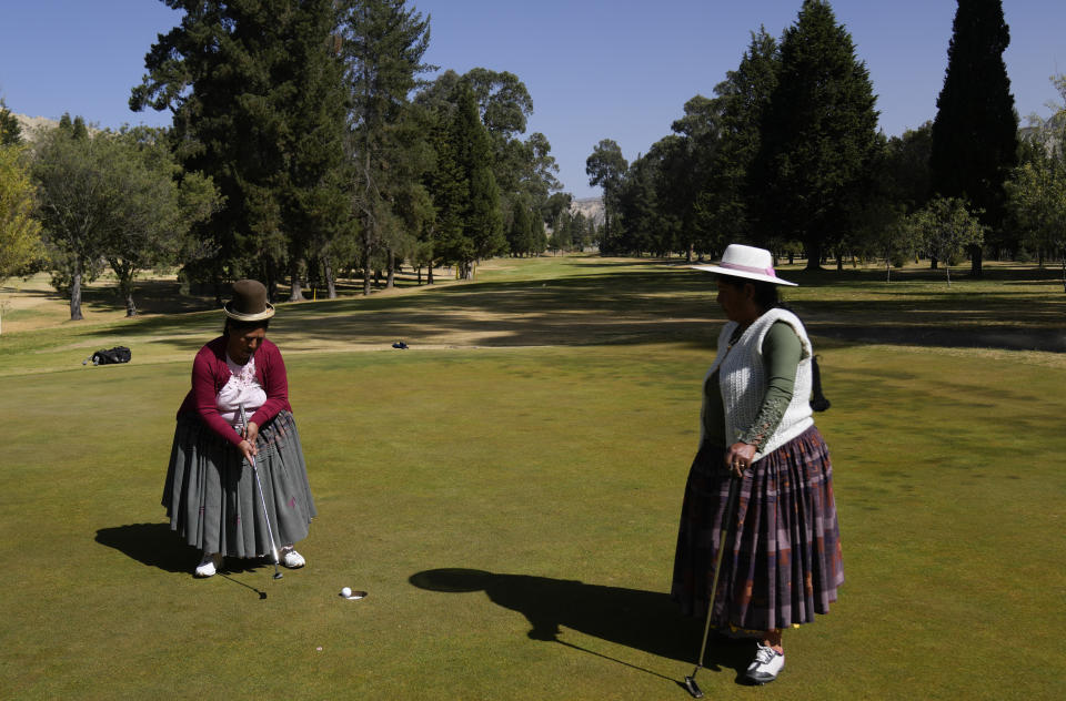 La indígena aymara Teresa Zárate, a la izquierda, lanza la pelota mientras Martha Mamani la mira durante el torneo de trabajadores en el Club de Golf La Paz de Mallasilla en las afueras de La Paz, Bolivia, el lunes 1 de agosto de 2022. (AP Foto/Juan Karita)